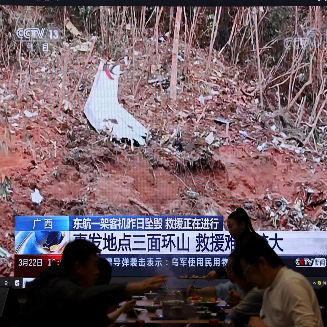 A screen shows news footage of plane debris at the site where a China Eastern Airlines Boeing 737-800 plane flying from Kunming to Guangzhou crashed in Wuzhou of Guangxi Zhuang Autonomous Region, while customers dine at a restaurant in Beijing, China March 22, 2022.