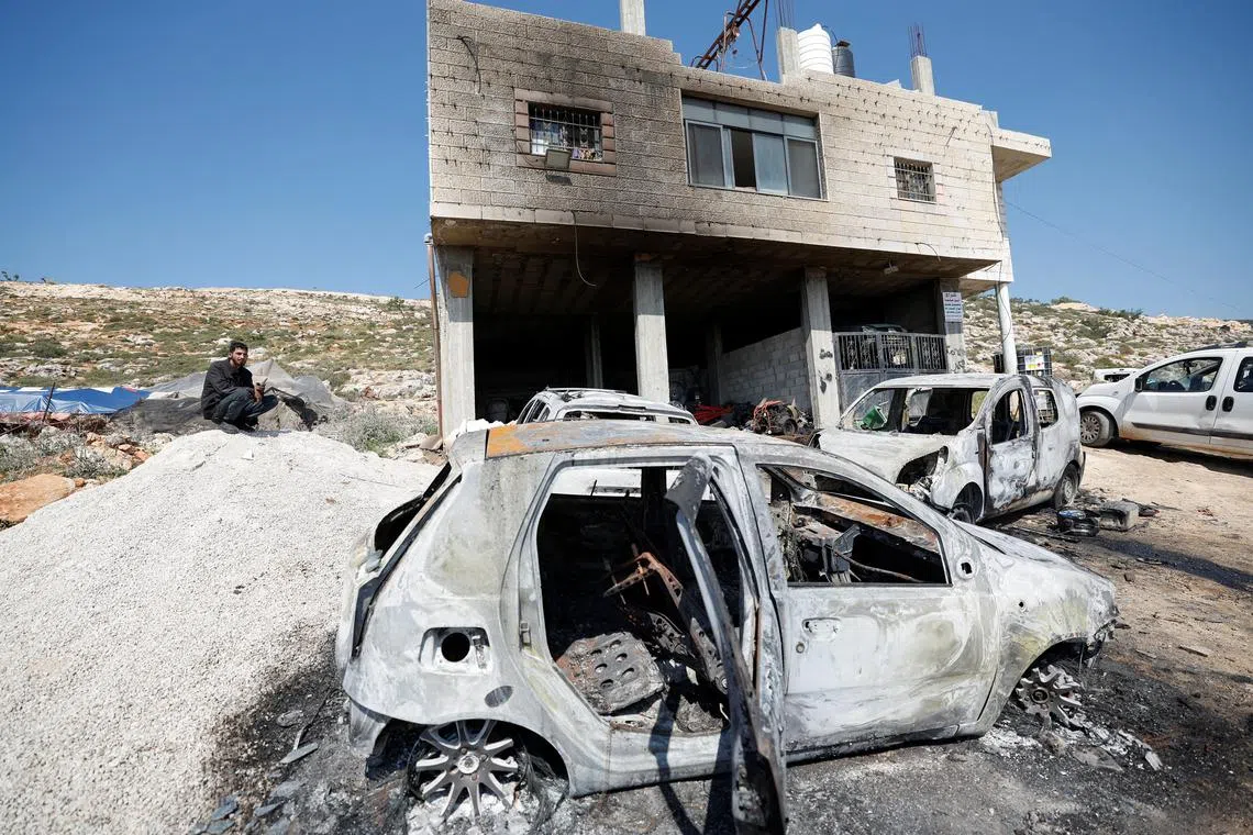 A Palestinian man sits near a damaged house and damaged cars after Israeli settlers attacked the village of al-Mughayyer, in the Israeli-occupied West Bank, April 13, 2024. REUTERS/Mohammed Torokman/File Photo