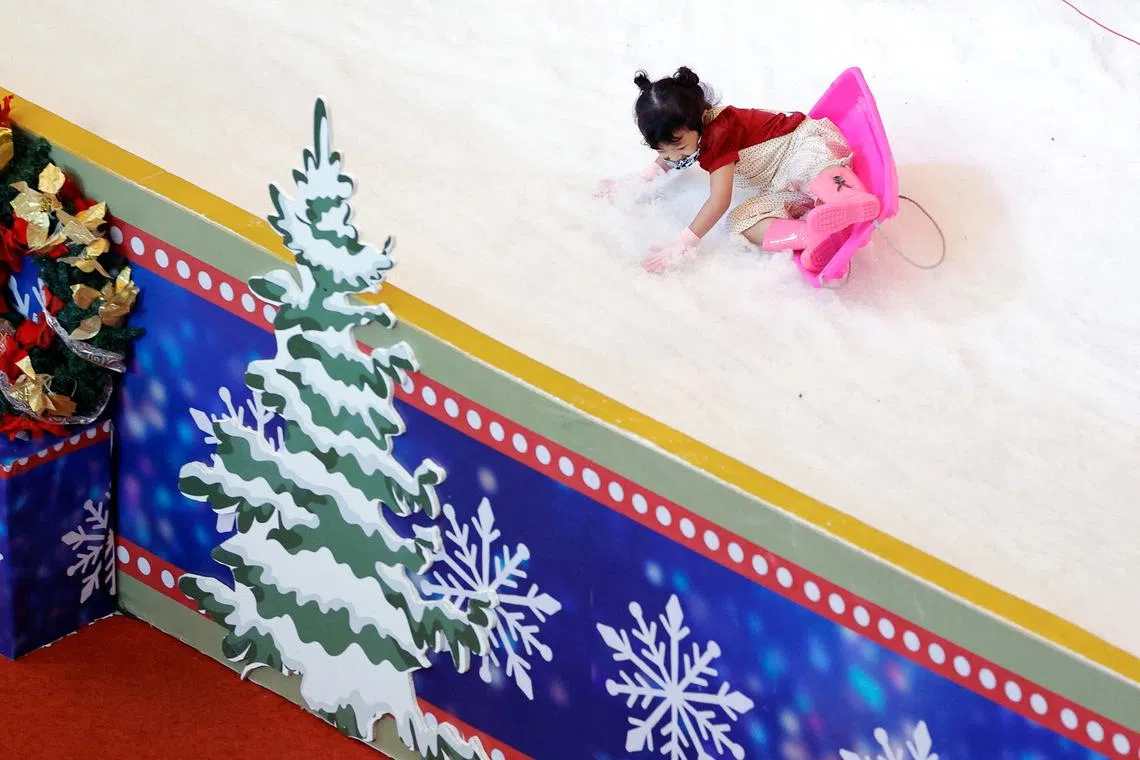 A girl falls from a sledge as she slides on artificial snow while playing at a playground inside the Taman Anggrek shopping mall, during the Christmas and New Year season in Jakarta, Indonesia, December 15, 2022. 