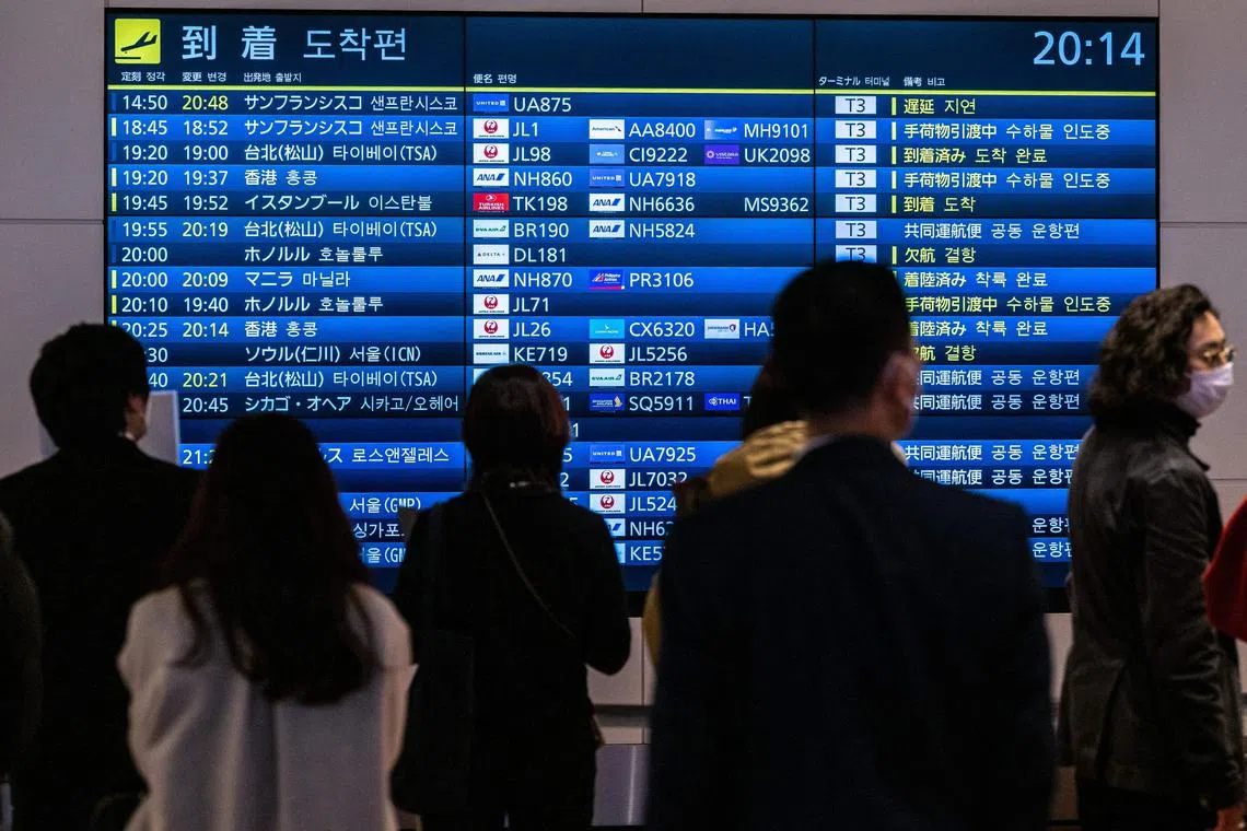 People wait in front a board showing international flight arrivals at Tokyo's Haneda international airport on December 28, 2022. - Hong Kong authorities on December 28 asked Japan to remove restrictions on direct flights from the city, which were imposed following the explosion of coronavirus cases in mainland China. (Photo by Philip FONG / AFP)