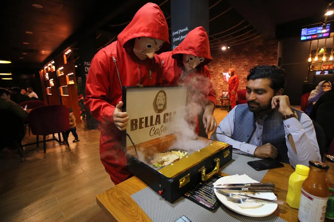 Bella Ciao Cafe staff, dressed up in the iconic red jumpsuit and Savlador Dali mask worn by the robbers in the Netflix series Money Heist (La Casa de Papel), serve food to a customer at the cafe in Peshawar, Pakistan, 07 November 2022.