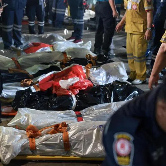 Members of emergency personnel working next to covered bodies at the site of a deadly fire at a pub in Bangkok, Thailand.