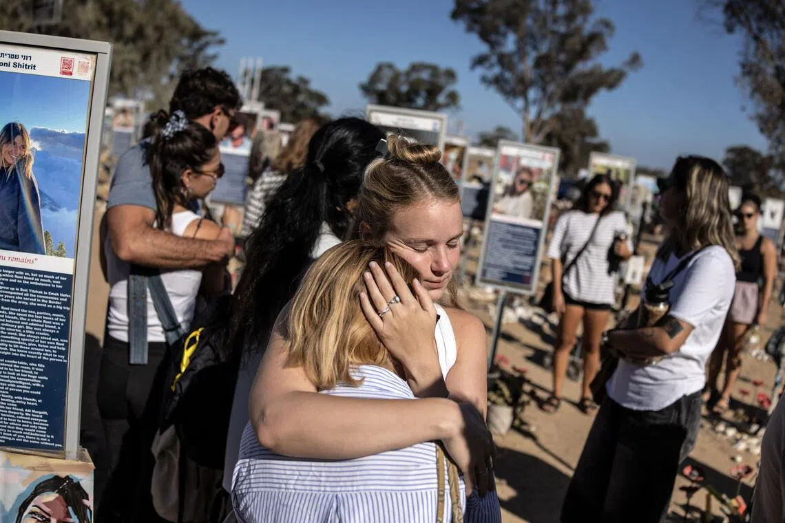 People embrace next to memorials of victims of a Hamas-led massacre at a music festival on Oct 7, 2023.

