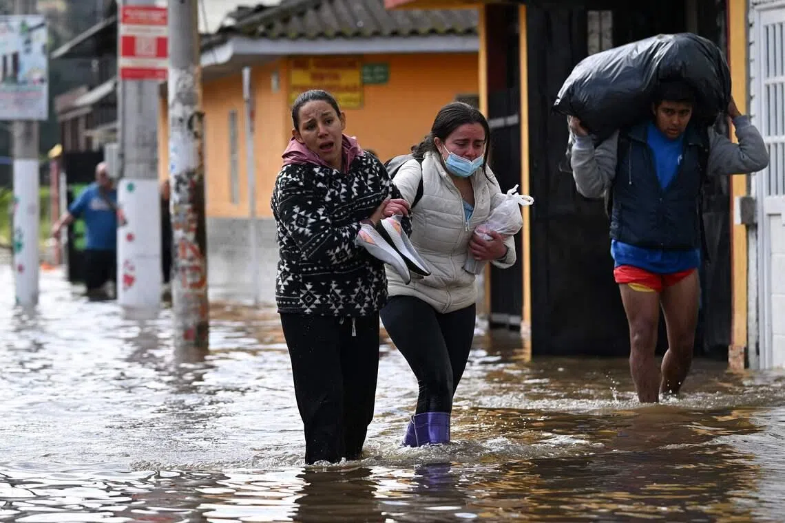 People walking through a flooded street while evacuating after heavy rains caused rivers to overflow in the Girardot neighborhood of Facatativa municipality, Cundinamarca department, Colombia, on March 19, 2026. 