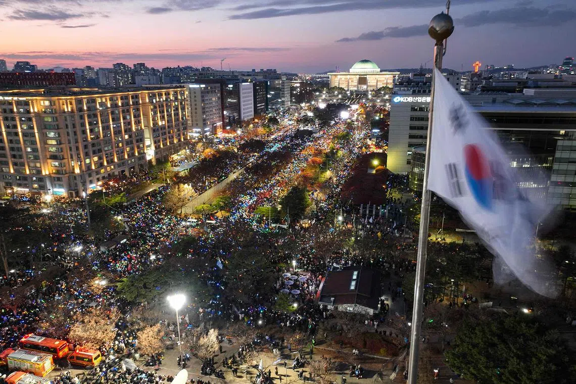 A South Korea flag flutters in the wind as a general view shows people taking part in a protest calling for the ouster of South Korea President Yoon Suk Yeol outside the National Assembly in Seoul on December 7, 2024. Yoon escaped impeachment on December 7 over his brief declaration of martial law, after lawmakers from his ruling party boycotted a vote despite huge protests outside parliament. The outcome disappointed the huge crowds -- numbering 150,000 according to police, one million according to organisers -- demonstrating outside parliament for Yoon's ouster. (Photo by YONHAP / AFP) / - South Korea OUT / NO ARCHIVES - RESTRICTED TO SUBSCRIPTION USE