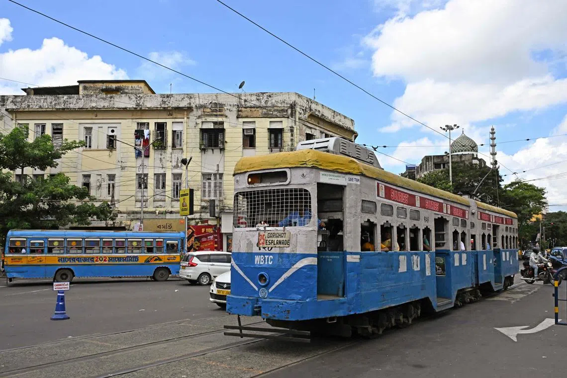 TOPSHOT - In this photo taken on September 8, 2024, passengers commute in a tram along a street in Kolkata. Introduced in the sprawling eastern city in 1873 during the early days of the imperial British Raj, trams in Kolkata were initially horse-drawn, then steam-driven. Electric-powered trams took to the streets in 1900. The single-storey trams -- painted in uniform stripes of bright blue and white, with a sunshine yellow top -- trundle at best at around 20 kilometres (12 miles) per hour, if not snarled in traffic blocking its route. (Photo by Dibyangshu SARKAR / AFP) / To go with "Asia's oldest operating trams see slow death in India" FOCUS
