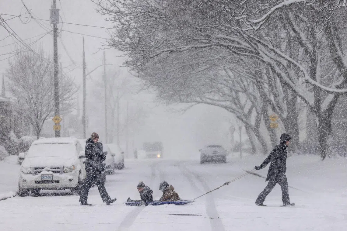 Laura Dejong pulls her nephews Caleb and Eli Fennema while their mother follows behind with infant Grace during a snow fall in Hamilton, Ontario, Canada January 25, 2023. 