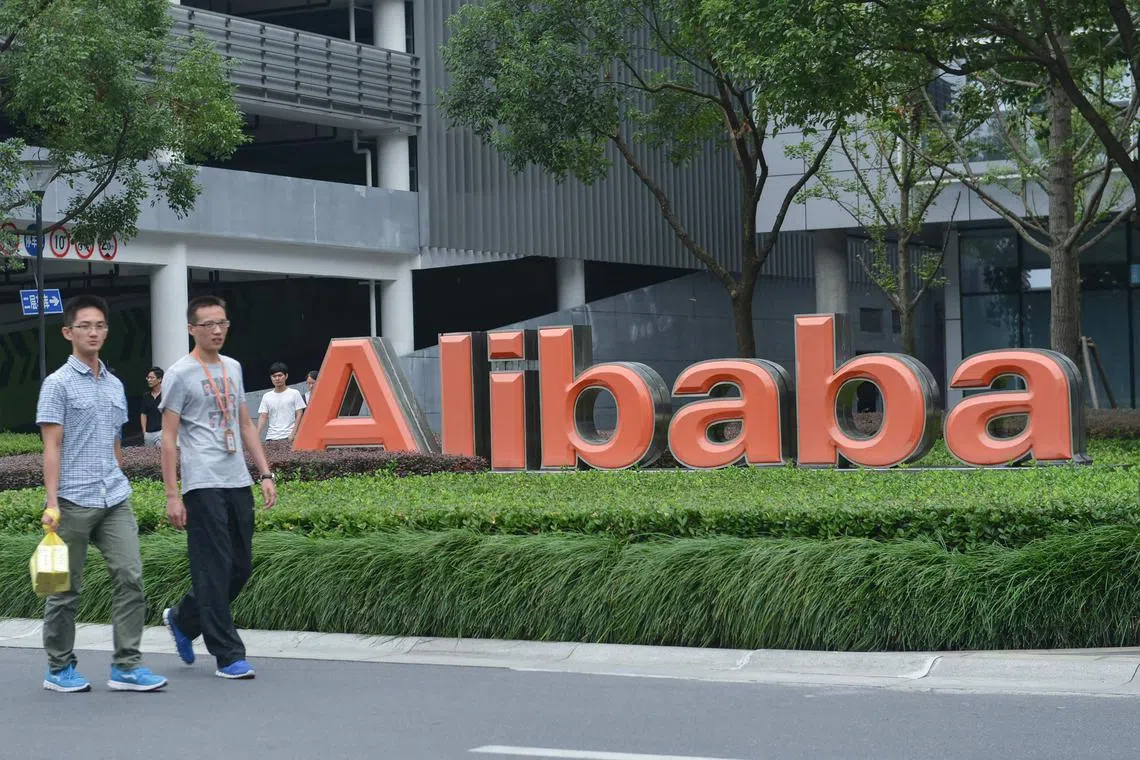 Staff members walking past the logo of Chinese e-commerce giant Alibaba at its headquarters in Hangzhou, in China's eastern Zhejiang province. - Alibaba announced on March 28, 2023, that it would split into six individual business groups in one of the most significant overhauls of a leading Chinese tech firm to date. (Photo by AFP) / China OUT