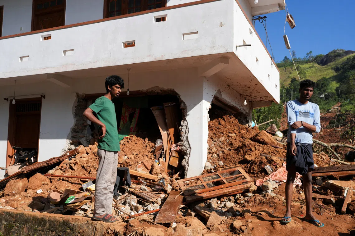 People stand next to debris near a damaged house after landslides caused by heavy rainfall following Cyclone Ditwah in Kandy, Sri Lanka, December 2, 2025. REUTERS/Thilina Kaluthotage