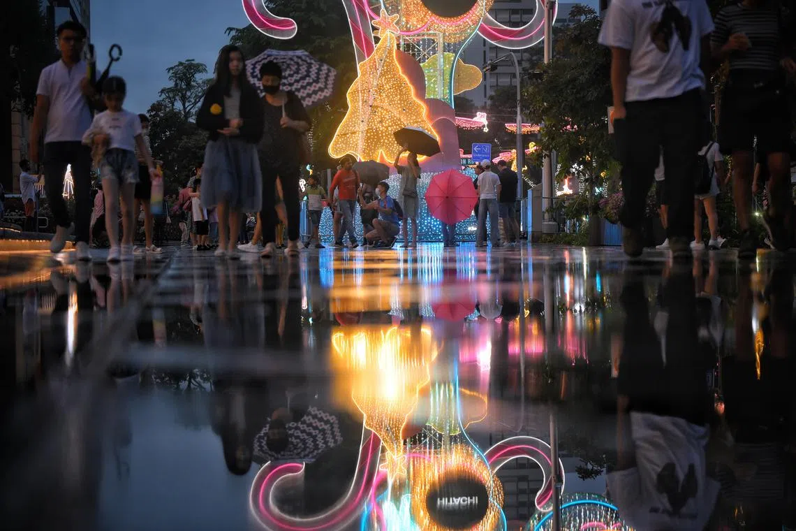 People taking pictures under rain next to Christmas decorations outside ION Orchard on Dec 23, 2023.