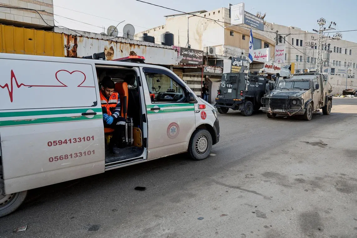 An emergency worker sits in an ambulance blocked by Israeli military vehicles during a raid. 