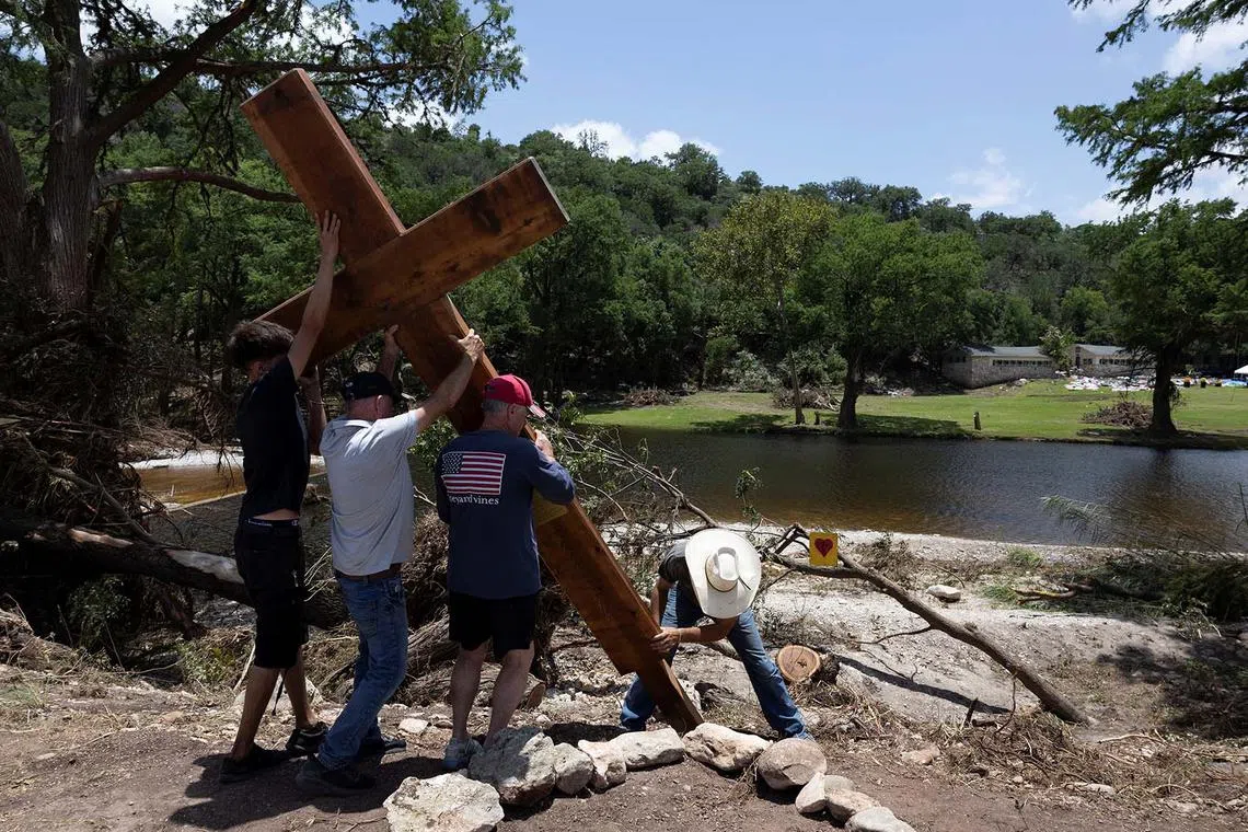 People placing a cross by the Guadalupe River, across from Camp Mystic, following deadly flooding, in Hunt, Texas, US, July 10, 2025. 