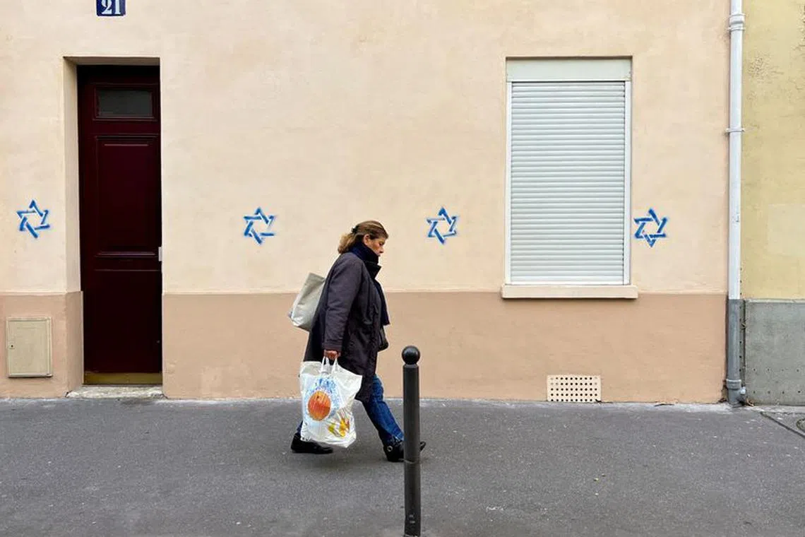FILE PHOTO: A woman walks past a building tagged with Stars of David in Paris, France, October 31, 2023. REUTERS/Lucien Libert/File Photo