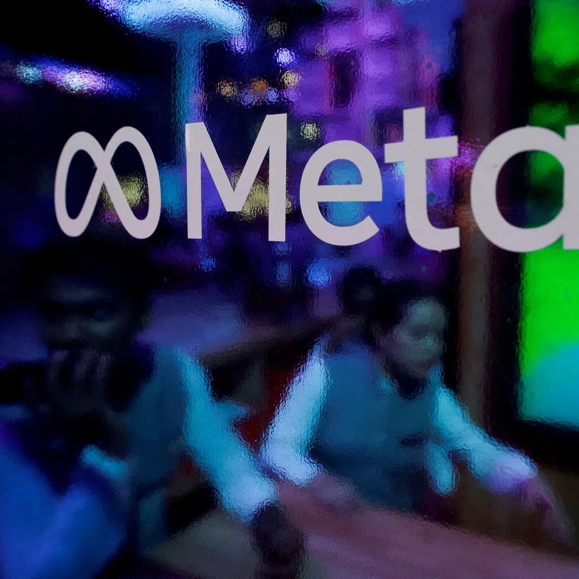 People are seen behind a logo of Meta Platforms, during a conference in Mumbai, India, on Sept 20, 2023.