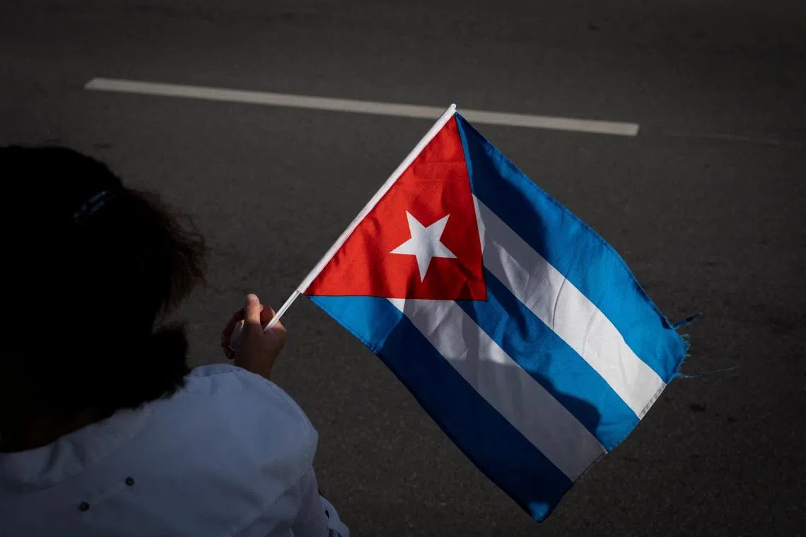 A woman holds a Cuban flag during a gathering outside Versailles Cafe after the U.S. Department of Justice announced criminal charges against former Cuban President Raul Castro, in Miami, Florida, U.S., May 20, 2026. REUTERS/Marco Bello