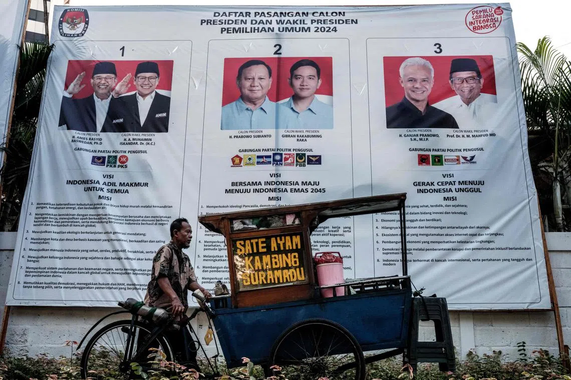 A street food vendor passes by a poster of three pairs of presidential and vice-presidential candidates, in Jakarta on December 20, 2023, ahead of the February 2024 Indonesian general election. (Photo by Yasuyoshi CHIBA / AFP)