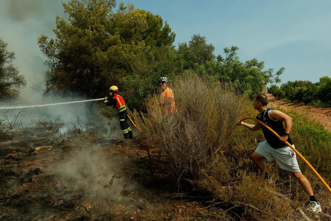 A firefighter uses a hose to extinguish flames during a wildfire in Betxi in Spain.
