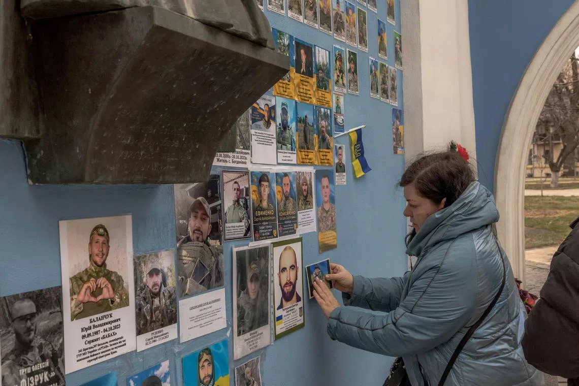 Olena places a photo of her husband Sergiy, a Ukrainian soldier killed fighting Russian troops, on the "Wall of Remembrance of the Fallen for Ukraine" in downtown Kyiv.