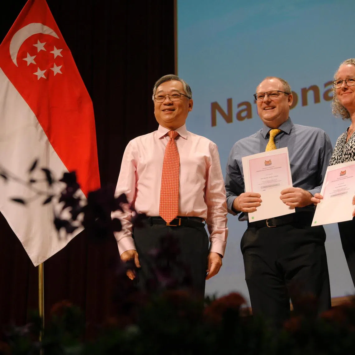 New Singaporean citizens Stacey Deborah Tucker (right), 51 and Nelius Strydom (Centre), 55, pictured with Gan Kim Yong, the Minister for Trade and Industry, pictured 
during the National Citizenship Ceremony 2023 held at ITE College West on August 13, 2023.