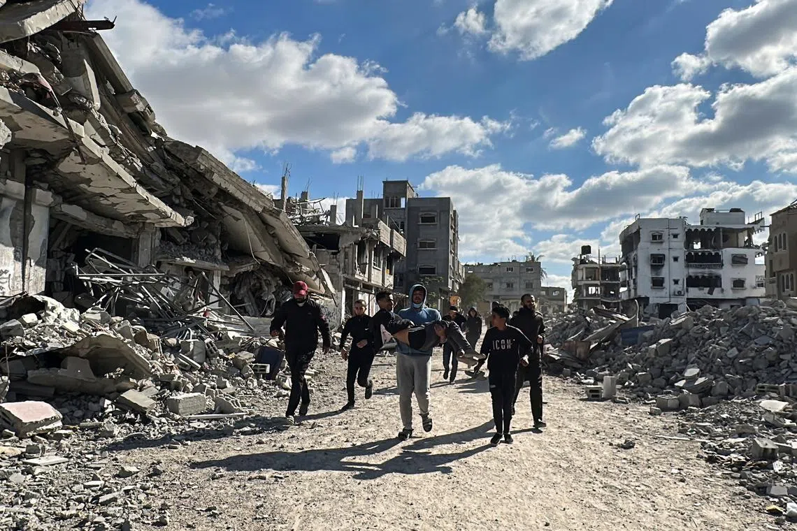 A man carries a wounded Palestinian as people walk past the rubble of houses and buildings destroyed during the war, following a ceasefire between Israel and Hamas, in Al-Bureij in the central Gaza Strip January 20, 2025. REUTERS/Khamis Saeed/File Photo