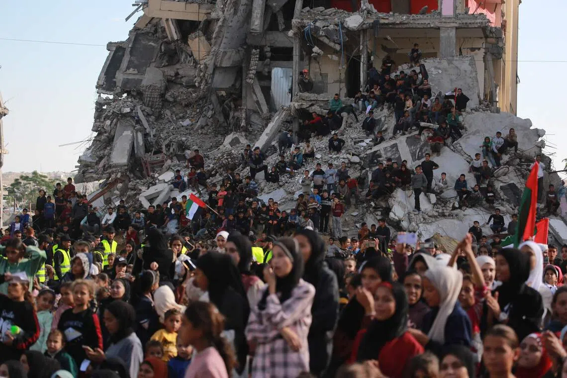 Palestinians gathering on the rubble of building destroyed by the Israeli military as they watch and celebrate the mass wedding of 54 couples dubbed the "The Dress of Joy", organised by the Al-Fares Al-Shahm Foundation, in Khan Yunis, southern Gaza Strip, on Dec 2, 2025. 