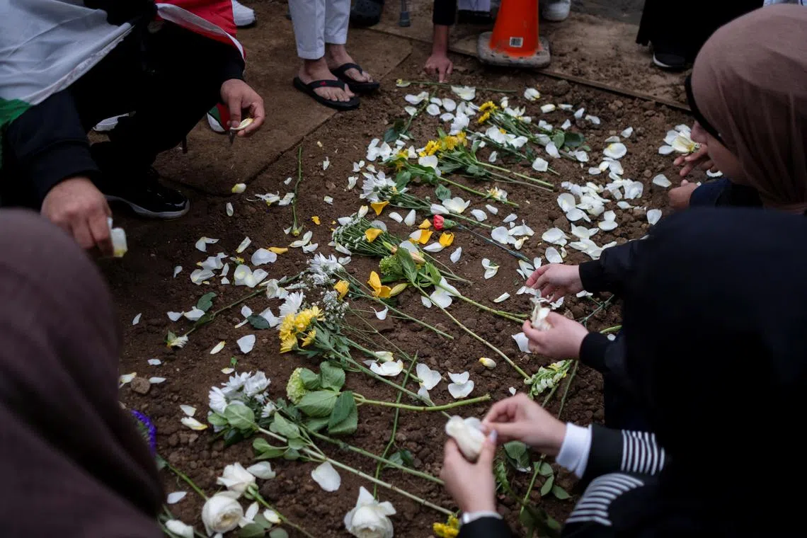 Mourners placing flowers at the grave of a Muslim boy who, according to police, was stabbed to death in an attack that targeted him and his mother for their religion and as a response to the war between Israel and Hamas. 