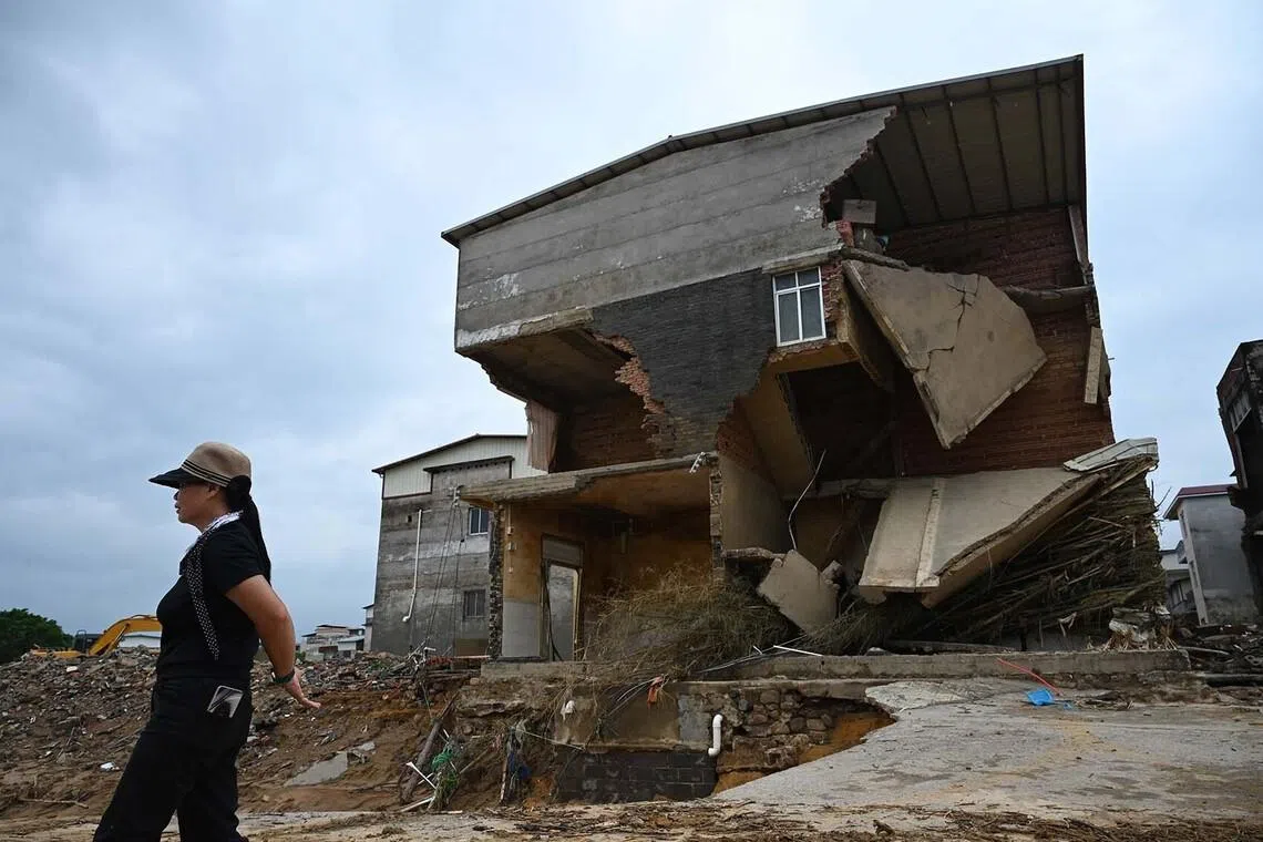TOPSHOT - A woman walks past houses which were damaged when the Liulan reservoir collapsed on July 6, in Liulan village, in Hengzhou city, in China’s southwest Guangxi region on July 8, 2026. Rescuers scoured flooded parts of China for survivors on July 8 after storms killed 17 people and caused dozens of rivers to overflow and a reservoir dam to burst, with officials warning of more rain. (Photo by GREG BAKER / AFP)