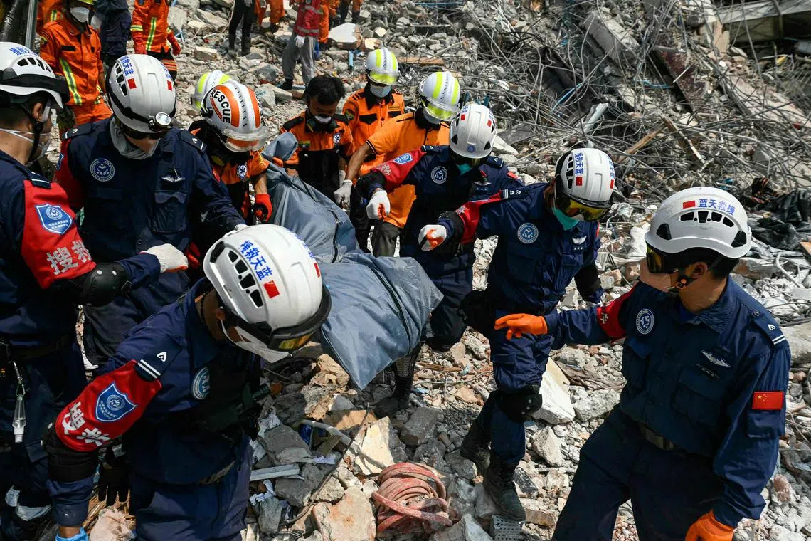 Myanmar and Chinese rescuers carry the body of a victim that was trapped under the rubble of the collapsed building 'Sky Villa Condominium development' in Mandalay on April 2, 2025, five days after a major earthquake struck central Myanmar. Days after a shallow 7.7-magnitude earthquake that killed more than 2,000 people, many people in Myanmar are still sleeping outdoors, either unable to return to ruined homes or afraid of further aftershocks. (Photo by Sai Aung MAIN / AFP)