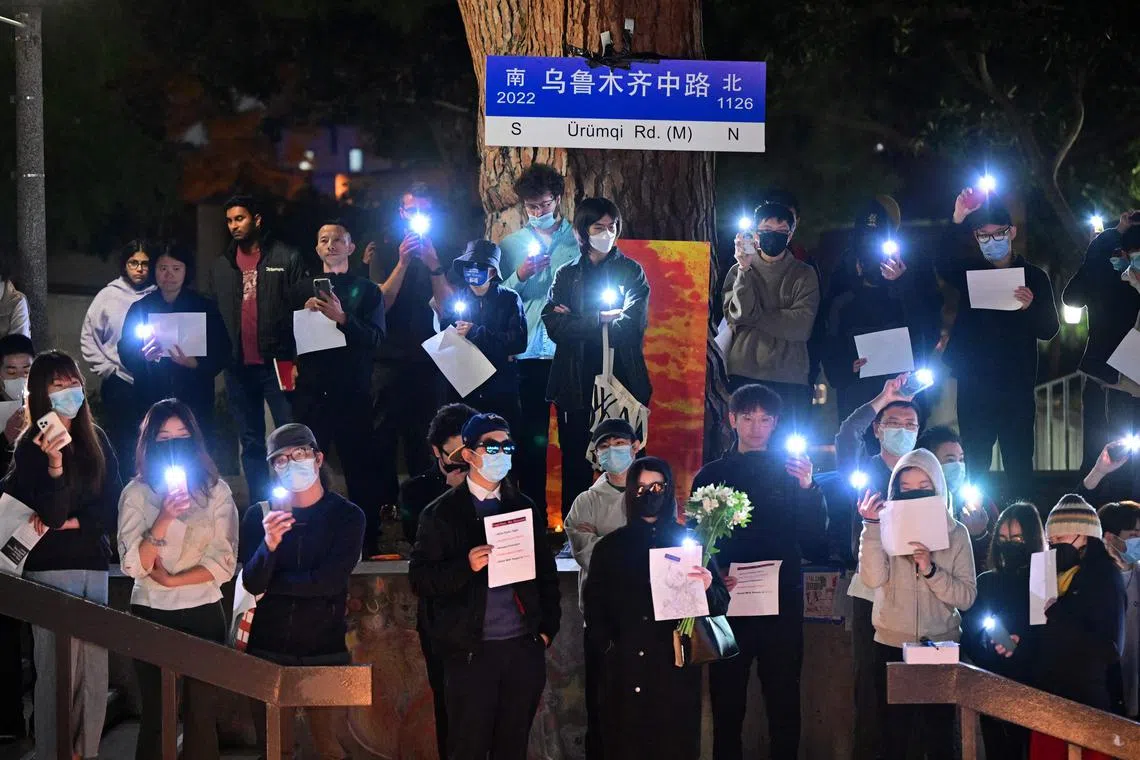 Standing beside a makeshift Urumuqi Road sign, people hold blank sheets of paper while protesting the deaths caused by an apartment complex fire in Urumqi, Xinjiang, China, at the Langson Library on the campus of the University of California, Irvine, in Irvine, California, on November 29, 2022. 