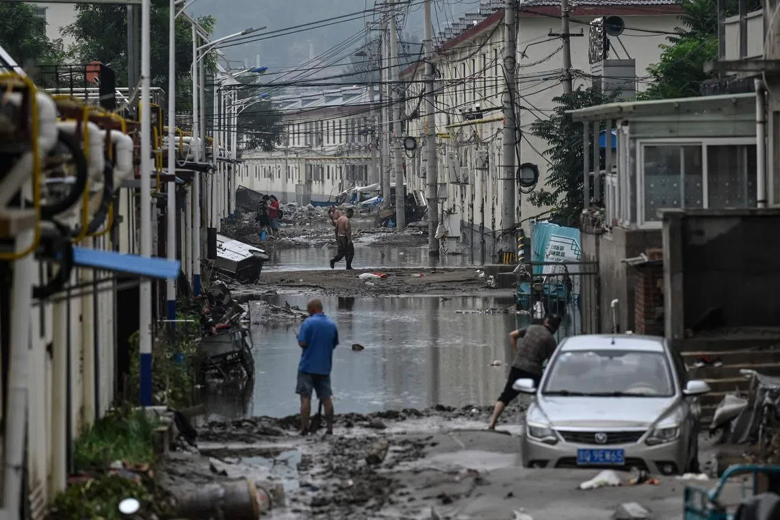 TOPSHOT - Local residents clean up the street in the aftermath of the flooding at a village following heavy rains in Beijing on August 3, 2023. Swathes of northern China were submerged in filthy floodwater on Wednesday after days of historic rainfall battered the capital city of Beijing and surrounding areas. (Photo by Jade Gao / AFP)