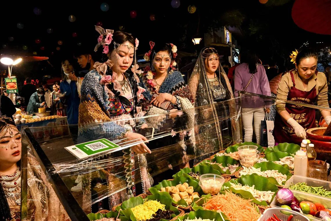 Women wearing traditional outfits as they look at food options in a night market in Jinghong city in Xishuangbanna Dai autonomous prefecture in China's south Yunnan province. 