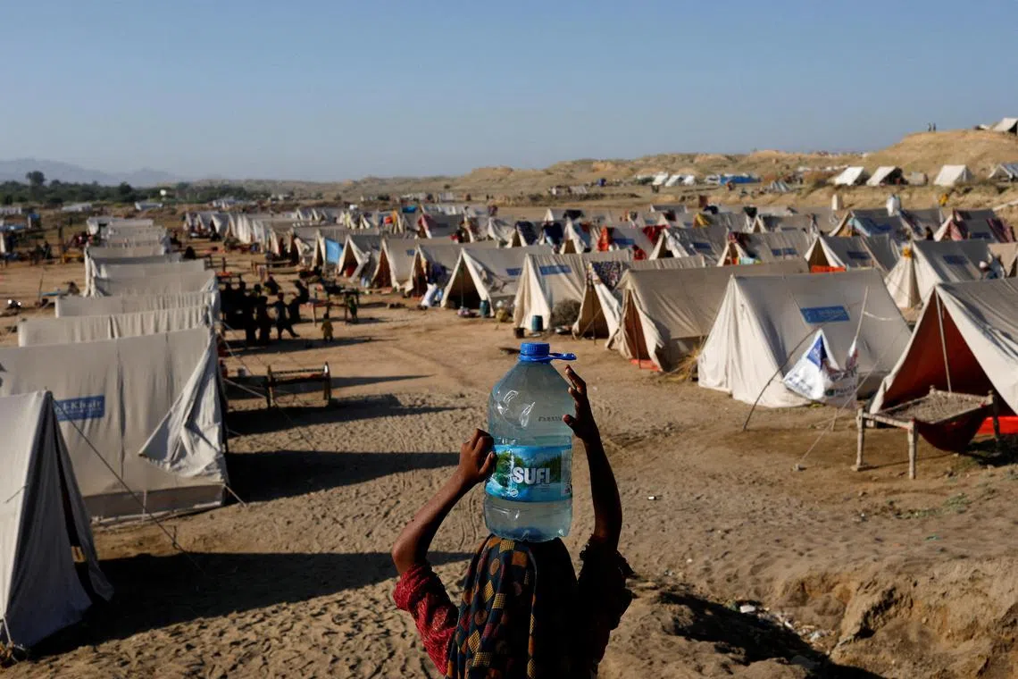A displaced girl carrying a bottle of water she filled from nearby flood-waters, as her family takes refuge in a camp, in Sehwan, Pakistan, on Sept 30, 2022.