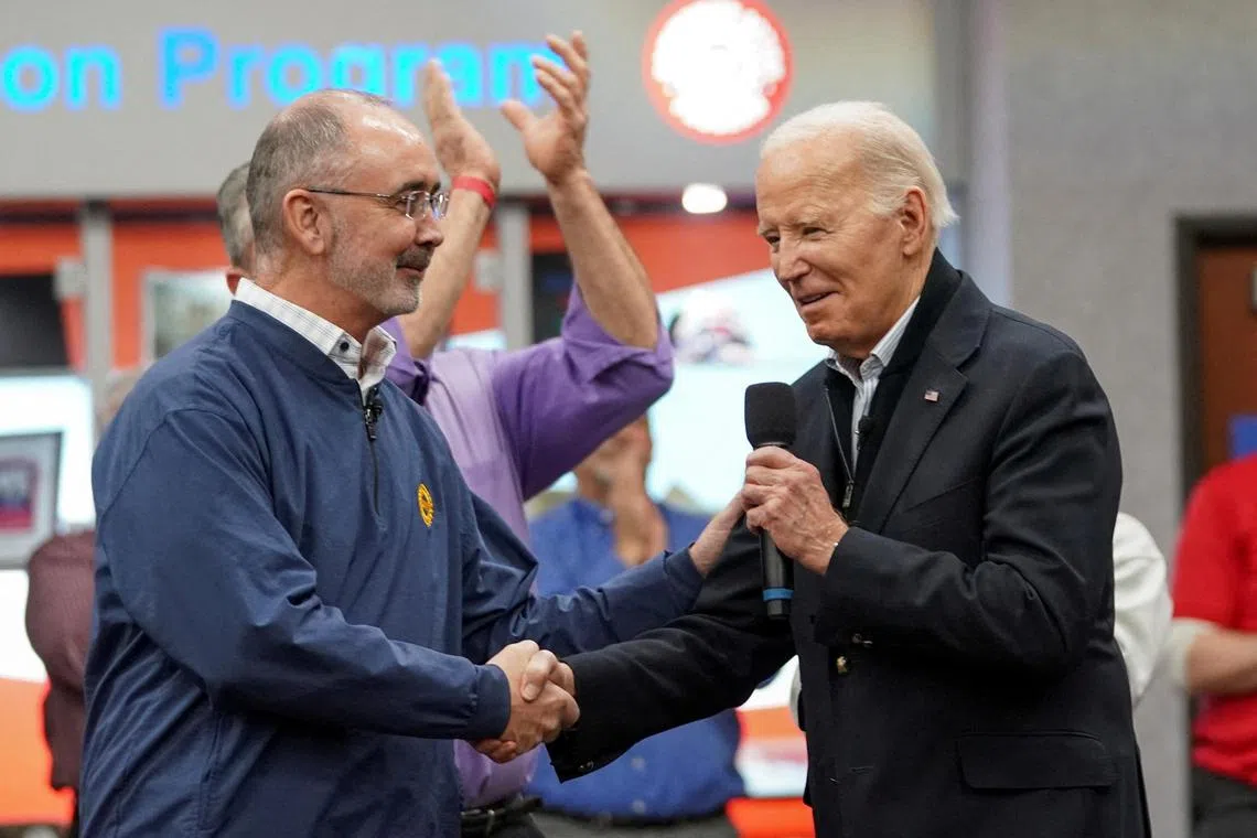 Mr Biden shakes hands with UAW president Shawn Fain, as they meet with auto workers .