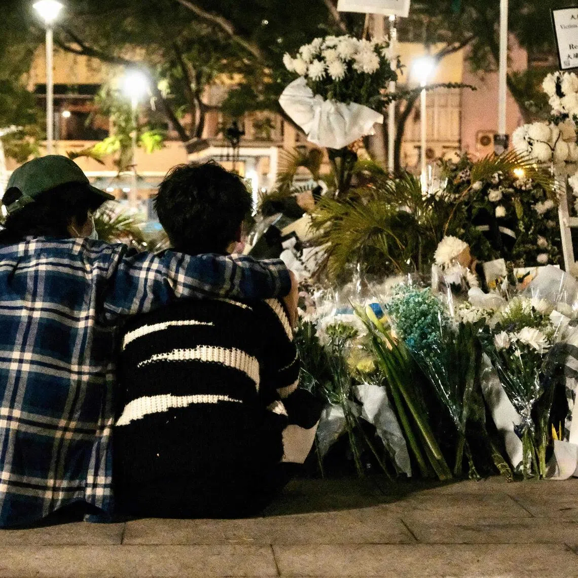 Volunteers sit in front of the flowers left by mourners for the victims of a deadly fire at the Wang Fuk Court residential estate in Tai Po district of Hong Kong on December 8, 2025.  PHOTO: AFP