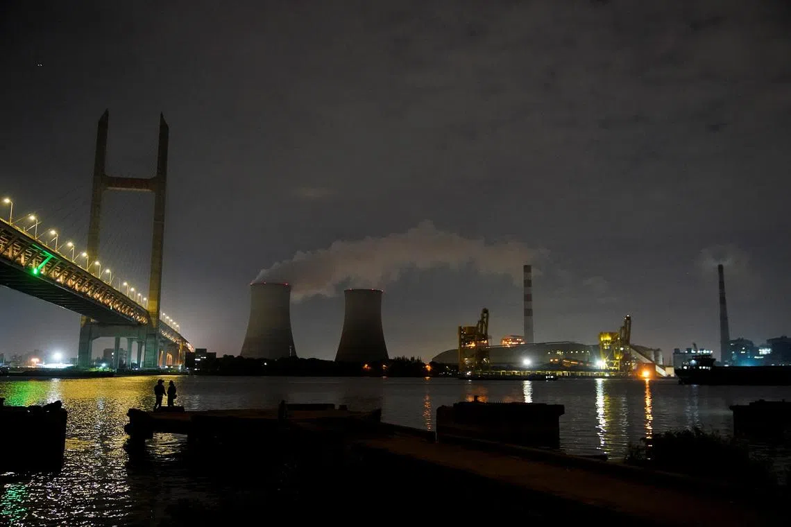 FILE PHOTO: People stand on a bank of the Huangpu river near a coal-fired power plant in Shanghai, China, October 14, 2021. REUTERS/Aly Song