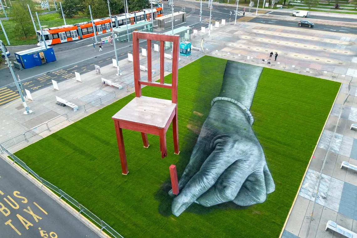 A land art painting called  "ALL OF US!", bringing attention to the plight of civilians in armed conflicts and made by Swiss French artist SAYPE, dialogues with the Broken Chair, on the Place des Nations in front of the United Nations in Geneva, Switzerland, Sept 11.
