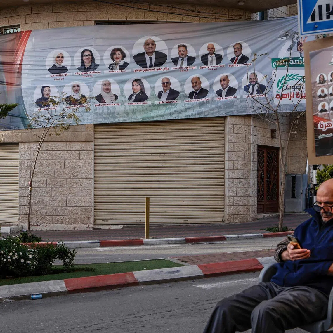 A man sits next to an election campaign banner showing candidates for the Ramallah and Al-Bireh governorates ahead of municipal elections, in the Israeli-occupied West Bank city of Ramallah.