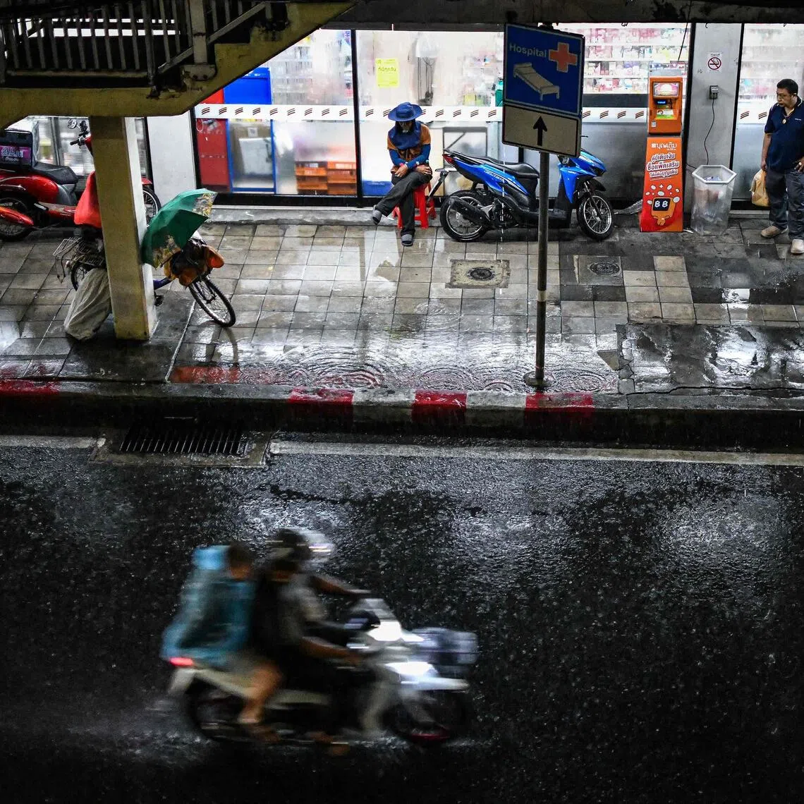 People take shelter from the rain on the sidewalk along Sukhumvit Road in Bangkok on Nov 1, 2025.