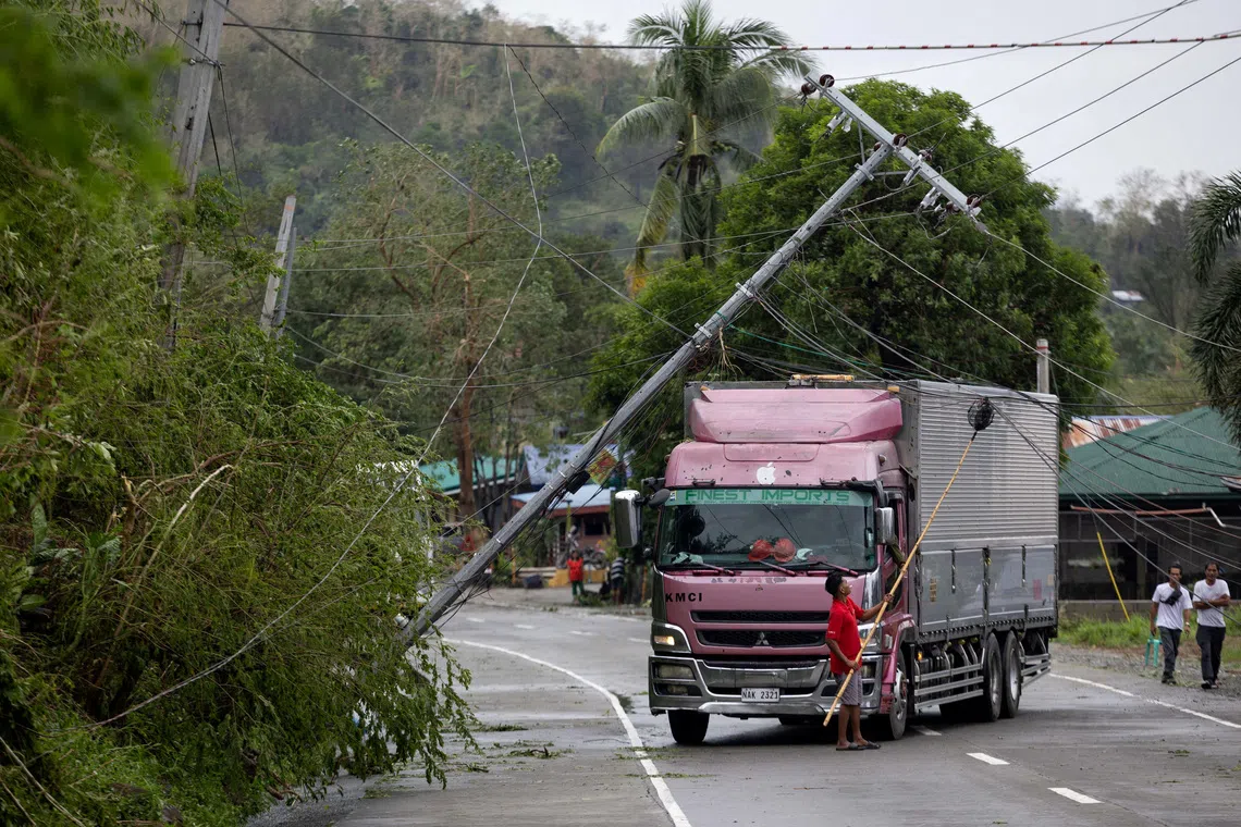 A man lifting wires with a fruit picker pole to assist a truck passing under a fallen post, in the aftermath of Typhoon Fung-wong, in Bagabag, Nueva Vizcaya, Philippines, on Nov 10, 2025. 