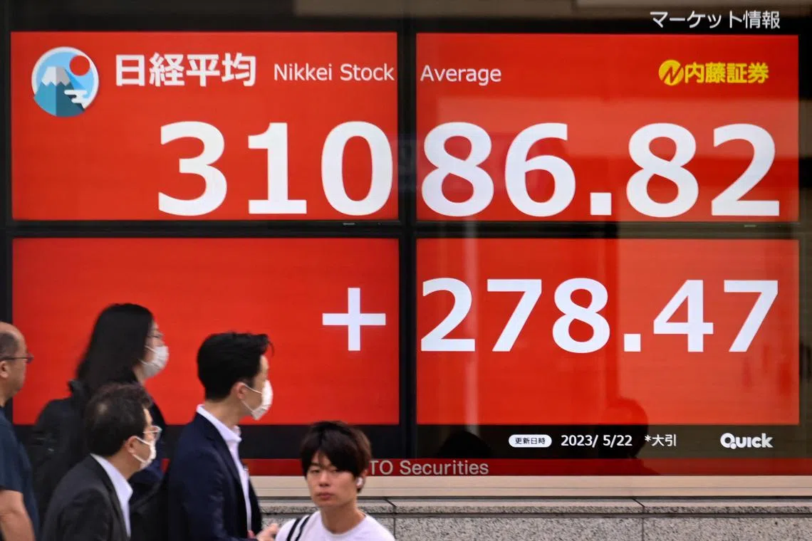 People pass an electronic board showing the closing numbers on the Tokyo Stock Exchange along a street in Tokyo on May 22, 2023. (Photo by Kazuhiro NOGI / AFP)