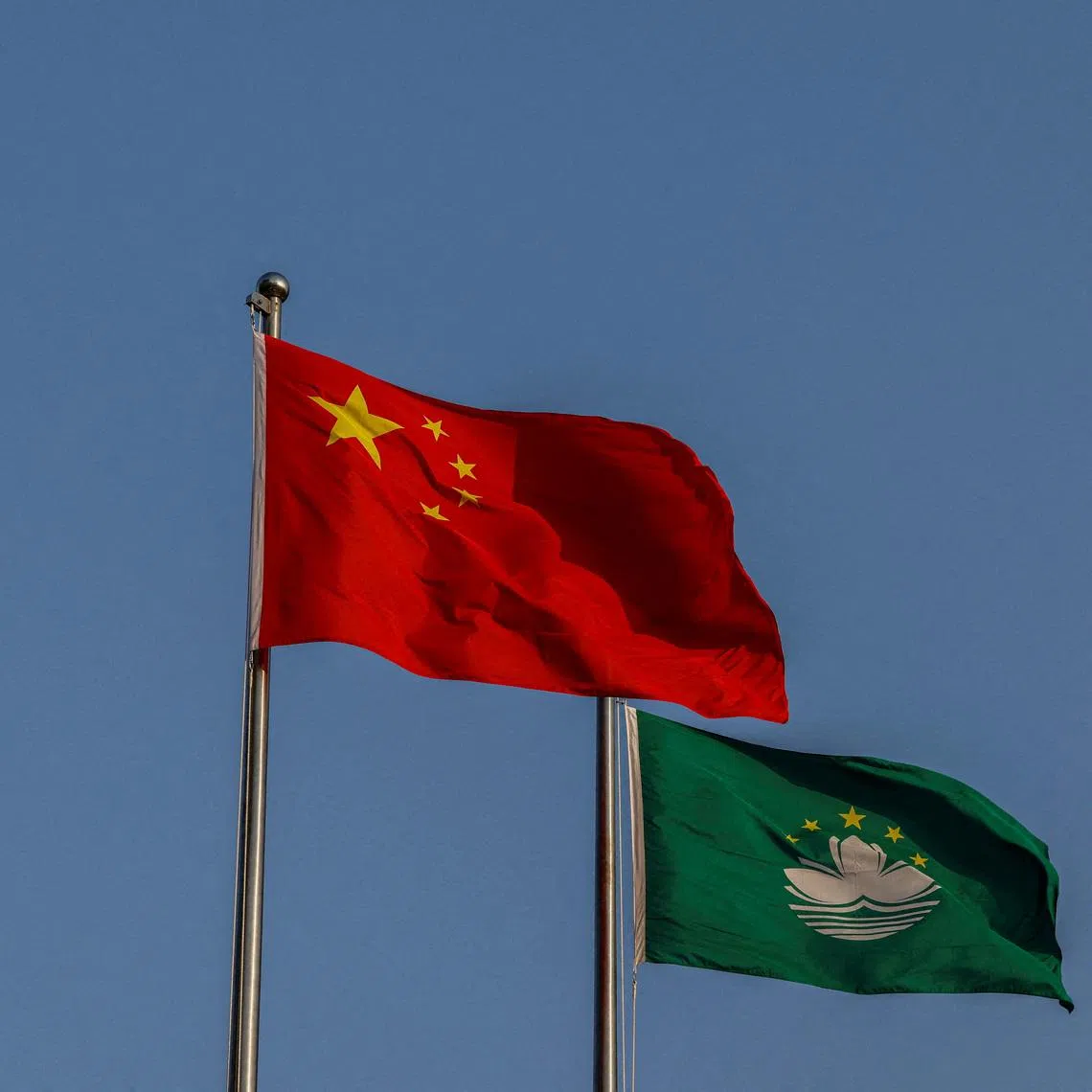FILE PHOTO: Chinese and Macau flags flutter during a flag-raising ceremony at the Golden Lotus Square to mark the 25th anniversary of Macau's handover from Portugal to China, in Macau, China December 20, 2024. REUTERS/Tyrone Siu/File Photo