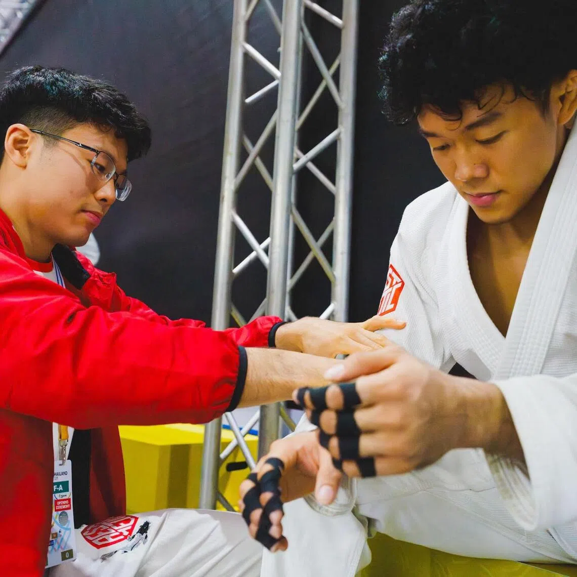 Singapore ju-jitsu exponent Paul Lim (left) helping his younger brother Noah Lim to tap his fingers before a fight at the 2025 SEA Games.