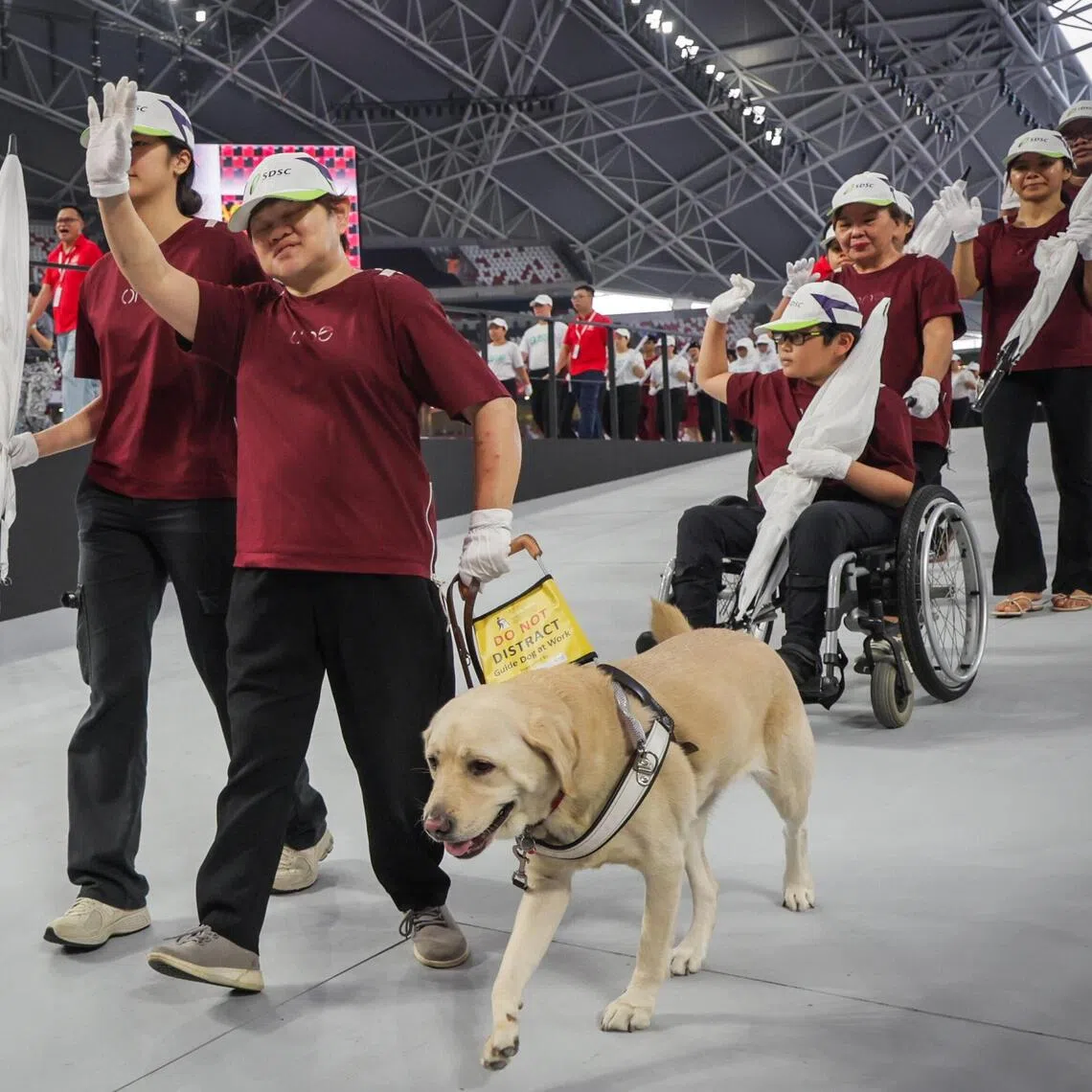 Lim Lee Lee (second from left, waving) and her guide dog, Hesta, together with Keith Pah and his grandmother, Tan Kim Choo, and others in the National Day Parade’s people with disabilities contingent, which has 21 members.