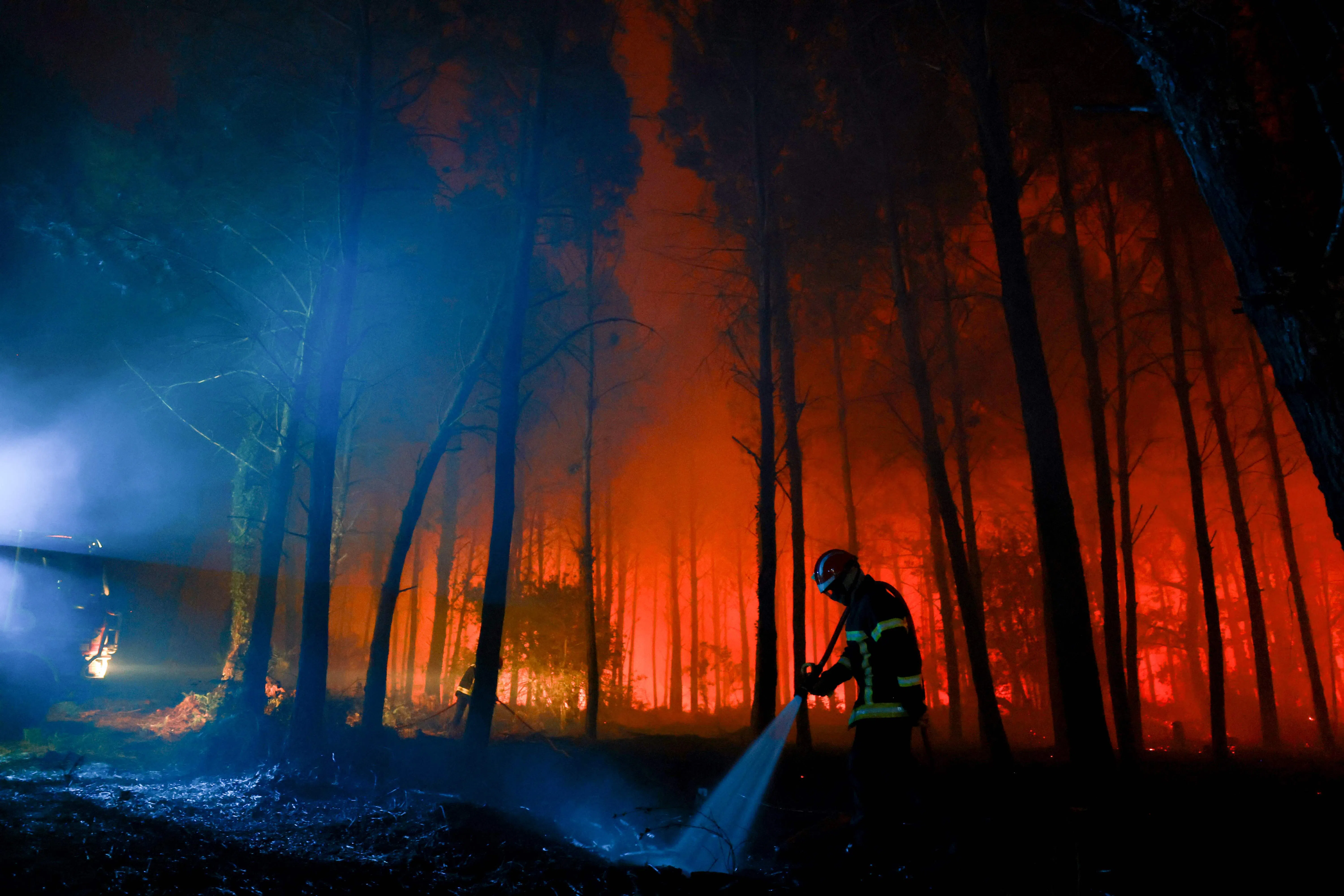 TOPSHOT - A firefighter hoses down the charred ground as flames continue to burn in the Landes forest in Luglon, southwestern France, in the early hours of August 14, 2026. The fire that broke out on August 13, 2026 in the Landes forest has now spread across 400 hectares, and 400 people "are being evacuated as a precautionary measure", according to the prefecture of this south-western department. (Photo by ROMAIN PERROCHEAU / AFP)