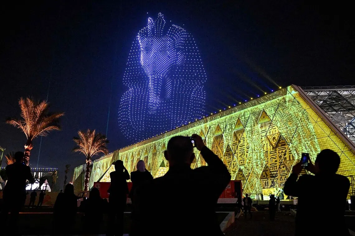TOPSHOT - Lightning effects depicting the funerary mask of ancient Egyptian King Tutankhamun light up the sky during the opening ceremony of the Grand Egyptian Museum (GEM) in Giza, on the southwestern outskirts of the capital Cairo on November 1, 2025. Near the ancient Pyramids of Giza just outside Cairo, the Grand Egyptian Museum is gearing up for a lavish opening on November 1, after two decades of delays. Massive statues and historic artefacts from the country's ancient civilisation will be on display across the 24,000 square metres (258,000 square feet) of permanent exhibition space. (Photo by Khaled DESOUKI / AFP)