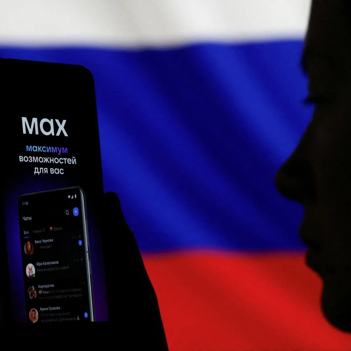 FILE PHOTO: A woman holds a smartphone displaying a web page of the Russian messenger application MAX next to a screen showing the state flag of Russia in this illustration taken September 4, 2025. REUTERS/Ramil Sitdikov/Illustration/File Photo