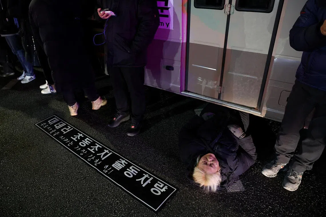 A woman lies on a road to block a vehicle transporting an army unit, on Dec 4, 2024, after South Korean President Yoon Suk Yeol declared martial law in Seoul the night before. 