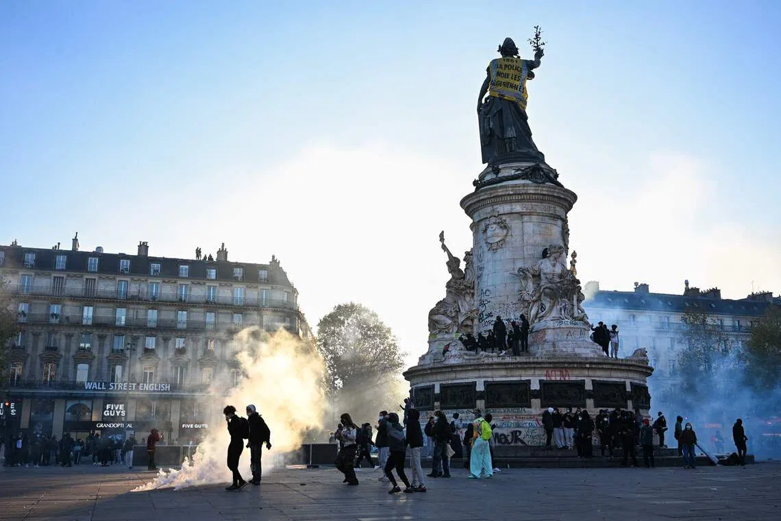 Protesters walk next to tear gas and the Statue de la Republique covered with a banner reading “1961 - Police drown Algerians” at Place de la Republique, Paris, on Oct 18.