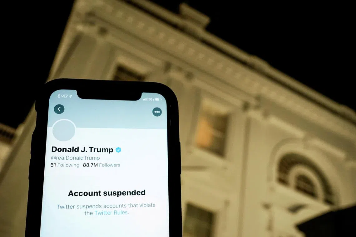 A photo illustration shows the suspended Twitter account of former president Donald Trump on a smartphone and a lit window at the White House.