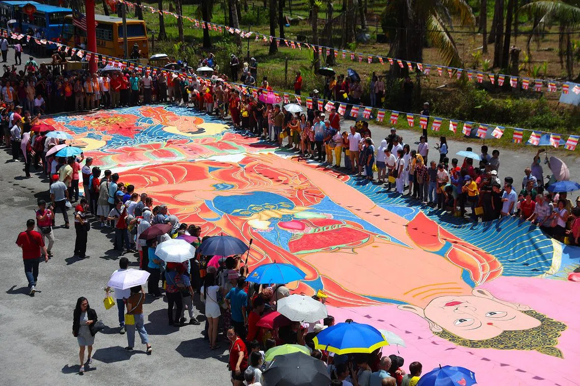 A 60m x 12m canvas of a thangka, a Tibetan Buddhist painting, is held up to enable devotees to walk under it to receive blessings and good luck from the Buddha for the coming year during the Vesak Day celebrations at the Enlightened Heart Tibetan Buddhist Temple in Ipoh, state of Perak, Malaysia, May 12, 2025. 